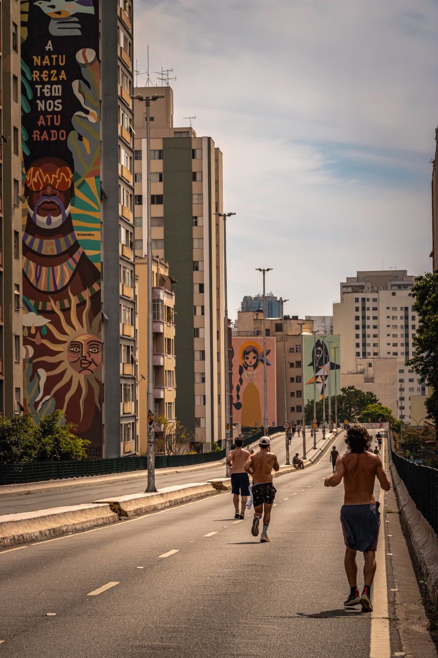 Vibrant street art with people running in São Paulo's urban landscape at sunset.